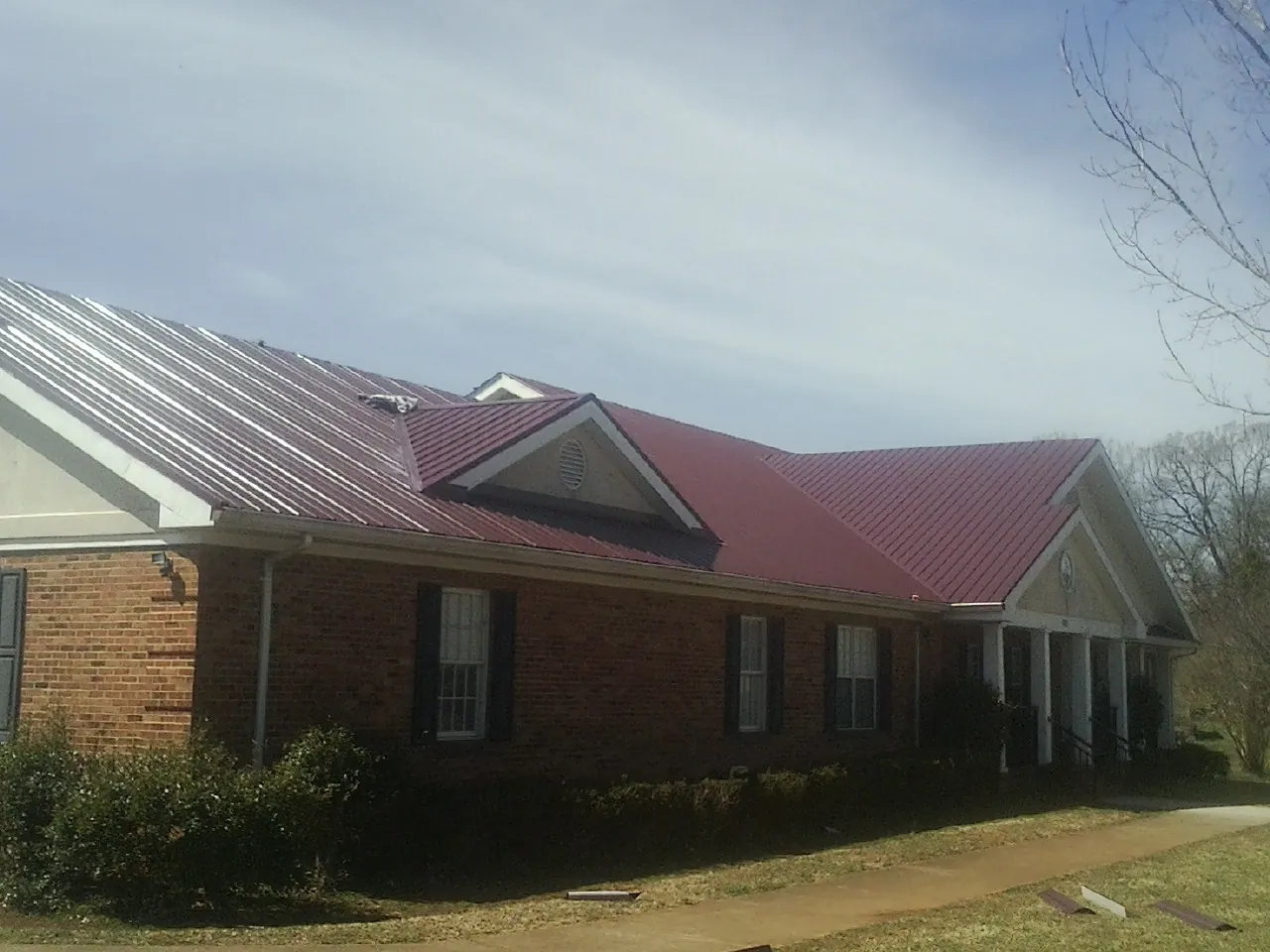 Red metal roof with gabled entries on a long brick building, from a Hail Damage Roof Repair job in Buckhannon