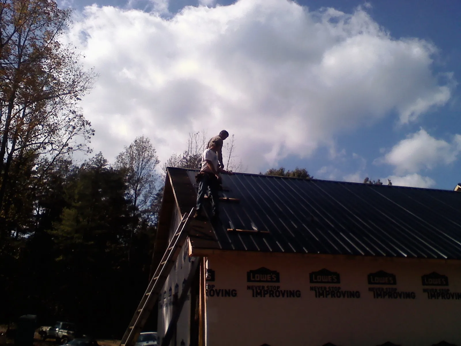 Roofer fastening dark metal panels high against a cloudy sky, from a Roof Inspection job in Buckhannon