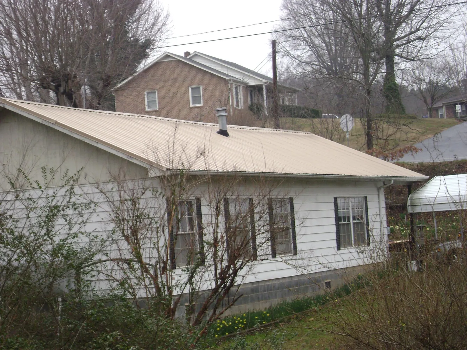 Tan metal roof on a white sided house set into a hillside — Commercial Roofing by Roofing Brothers in Buckhannon