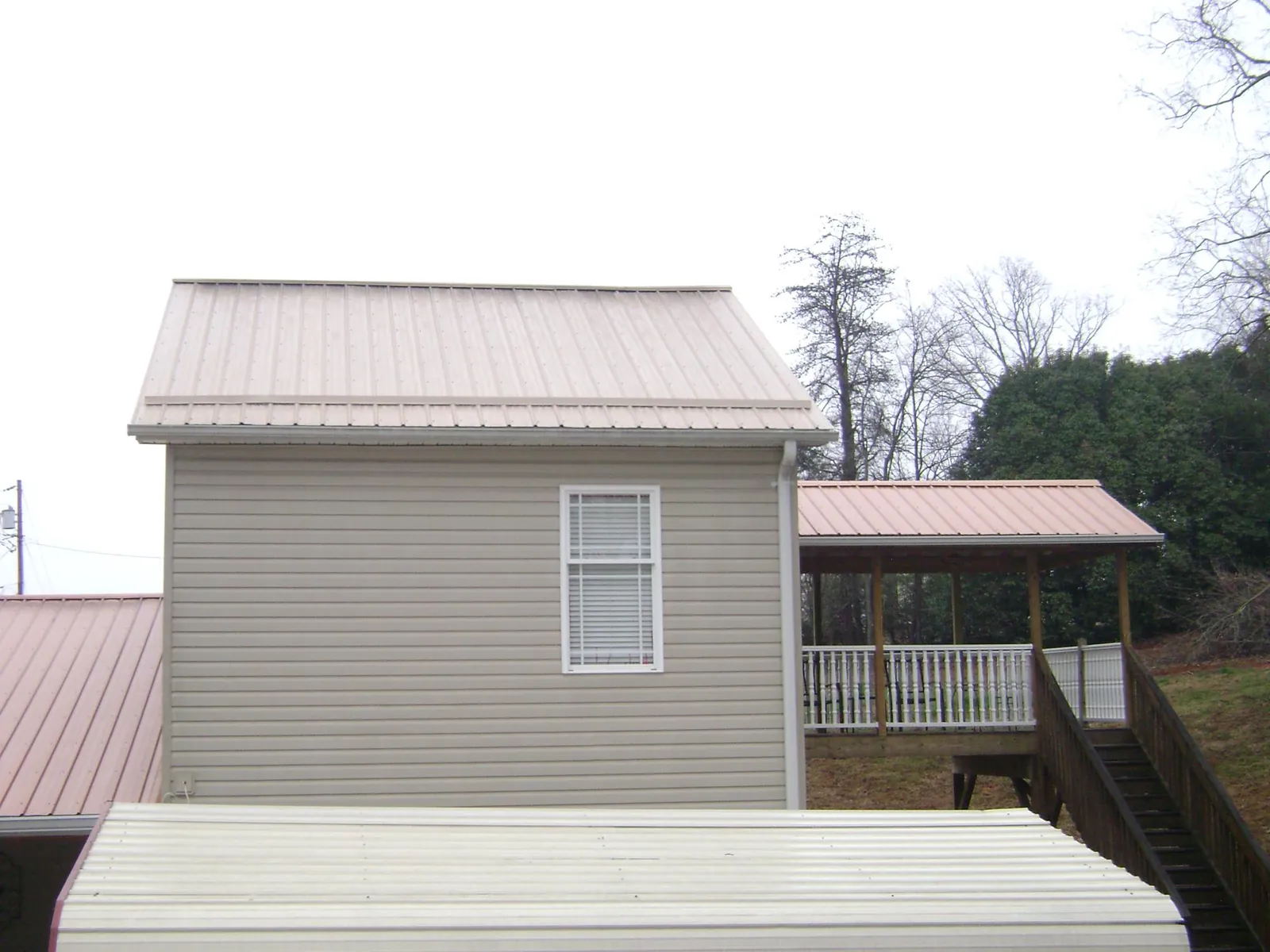 Tan metal roofs on a two story addition and attached porch, from a Roof Replacement job in Buckhannon